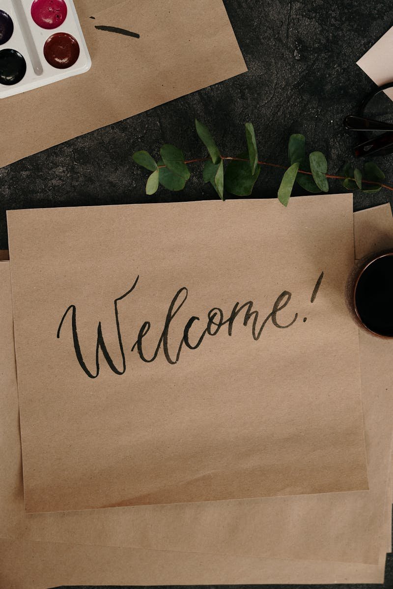 A creative workspace featuring calligraphy, envelopes, and art supplies for crafting personalized welcome cards.